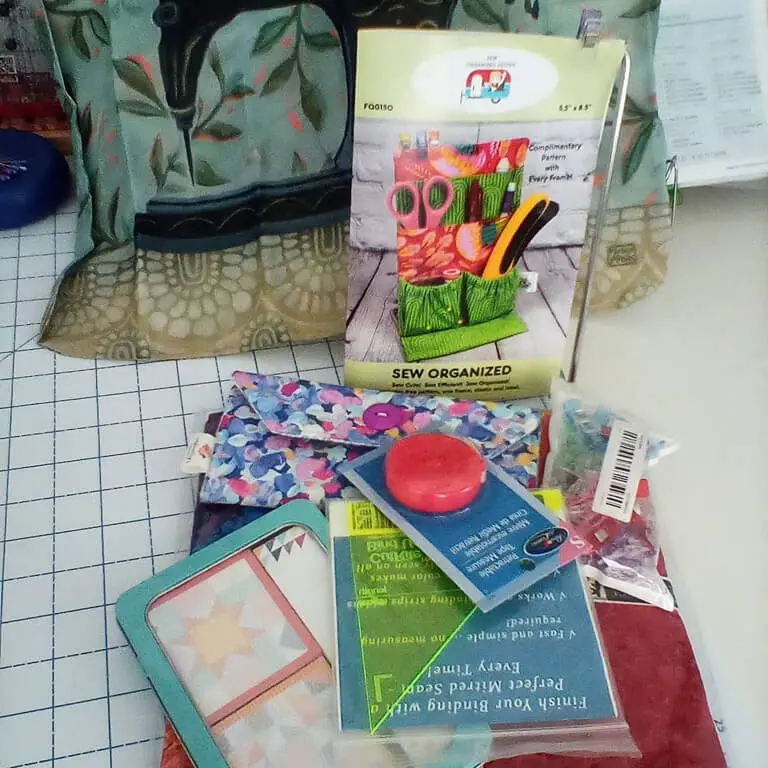 Table topped with a variety of sewing supplies, including a bag, scissors, a book, a box, a cover, a paper