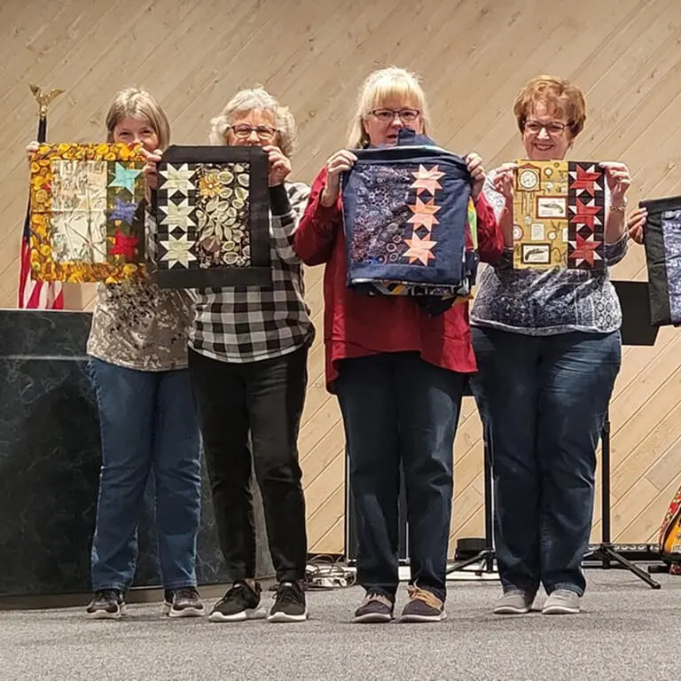 Group of four women standing next to each other, each holding up a quilt