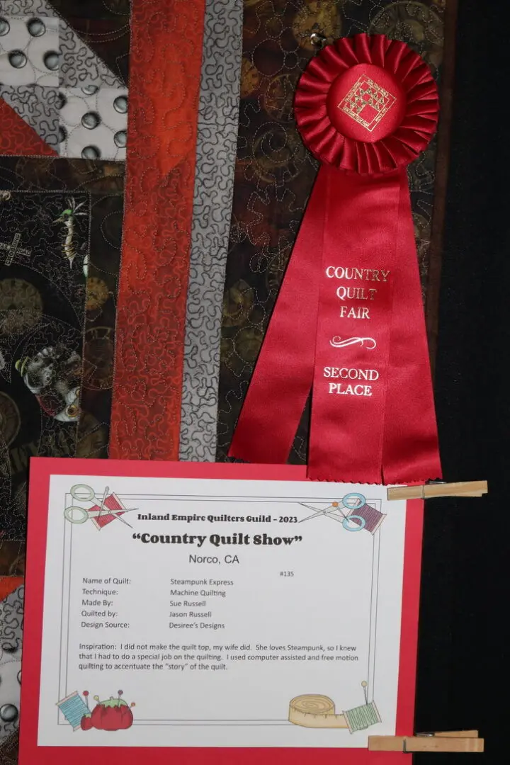 Red ribbon with a red rosette on top of it, attached to a board with clips, against a black background