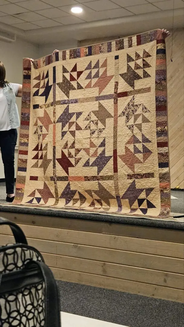 Woman standing on a stage, holding up a large quilt