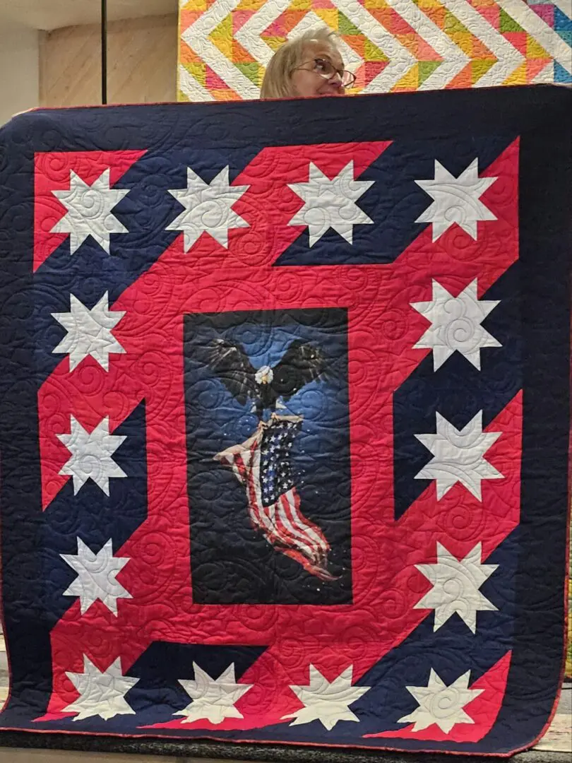 Woman holding up a quilt with an eagle on it, which is part of the 2018