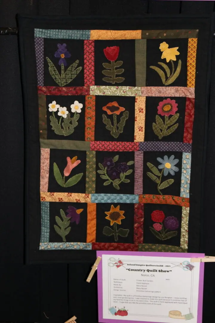 Quilted wall hanging on a black wall next to a piece of paper with text and pictures of flowers