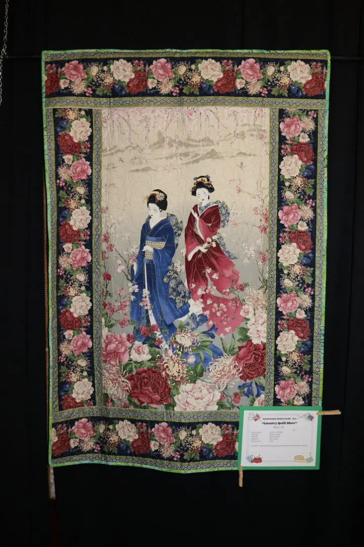 Chinese silk embroidered wall hanging depicting two geishas in a garden, with a paper attached to the cloth