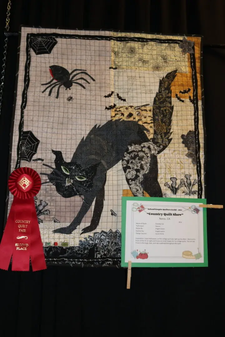 Quilted wall hanging with a black cat and a red ribbon on it, along with a paper with text