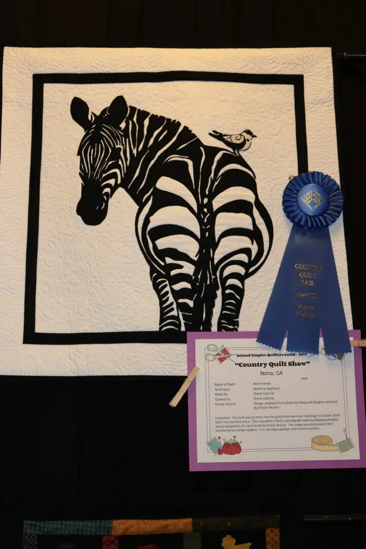 Quilted wall hanging with a zebra and a bird on it, along with a paper with text and a ribbon