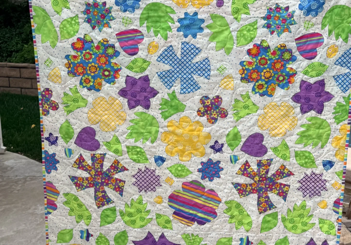 Woman holding up a vibrant quilt with a variety of colorful flowers on it